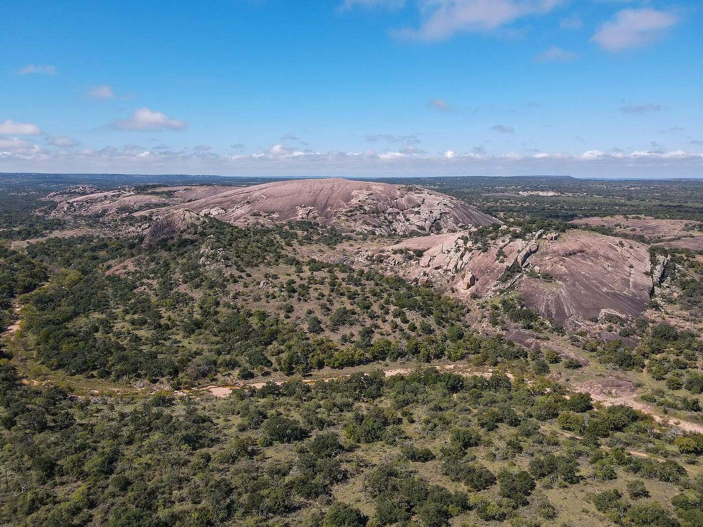 Aerial view of a large pink granite dome rising out of green Hill Country scrub