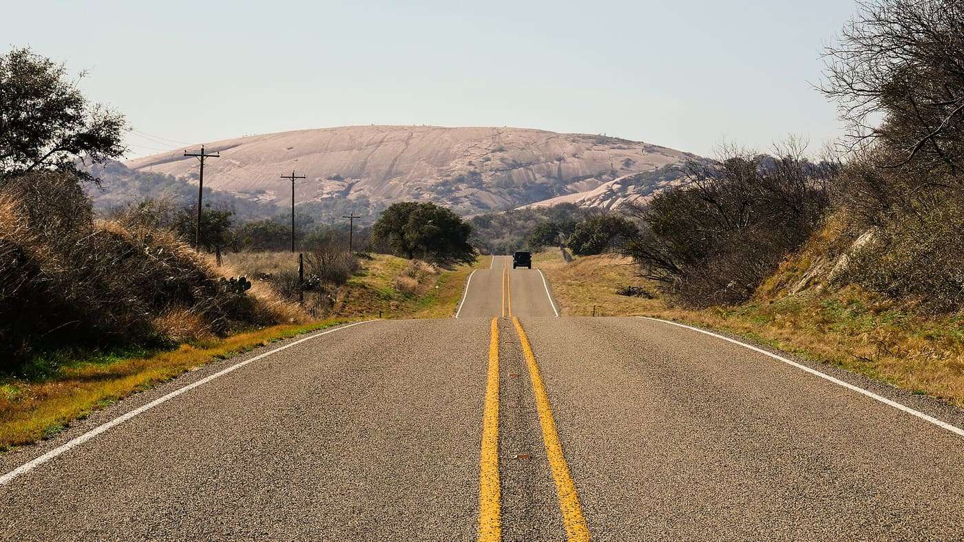 Two-lane highway leading toward a low pink granite dome